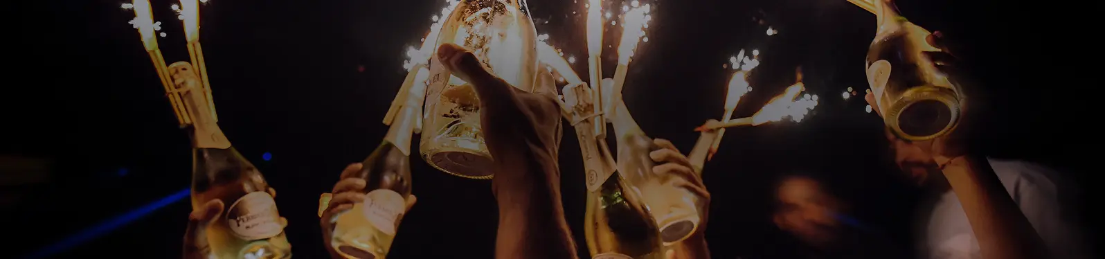 Champagne bottles with sparklers raised in celebration at a crowded nightclub.