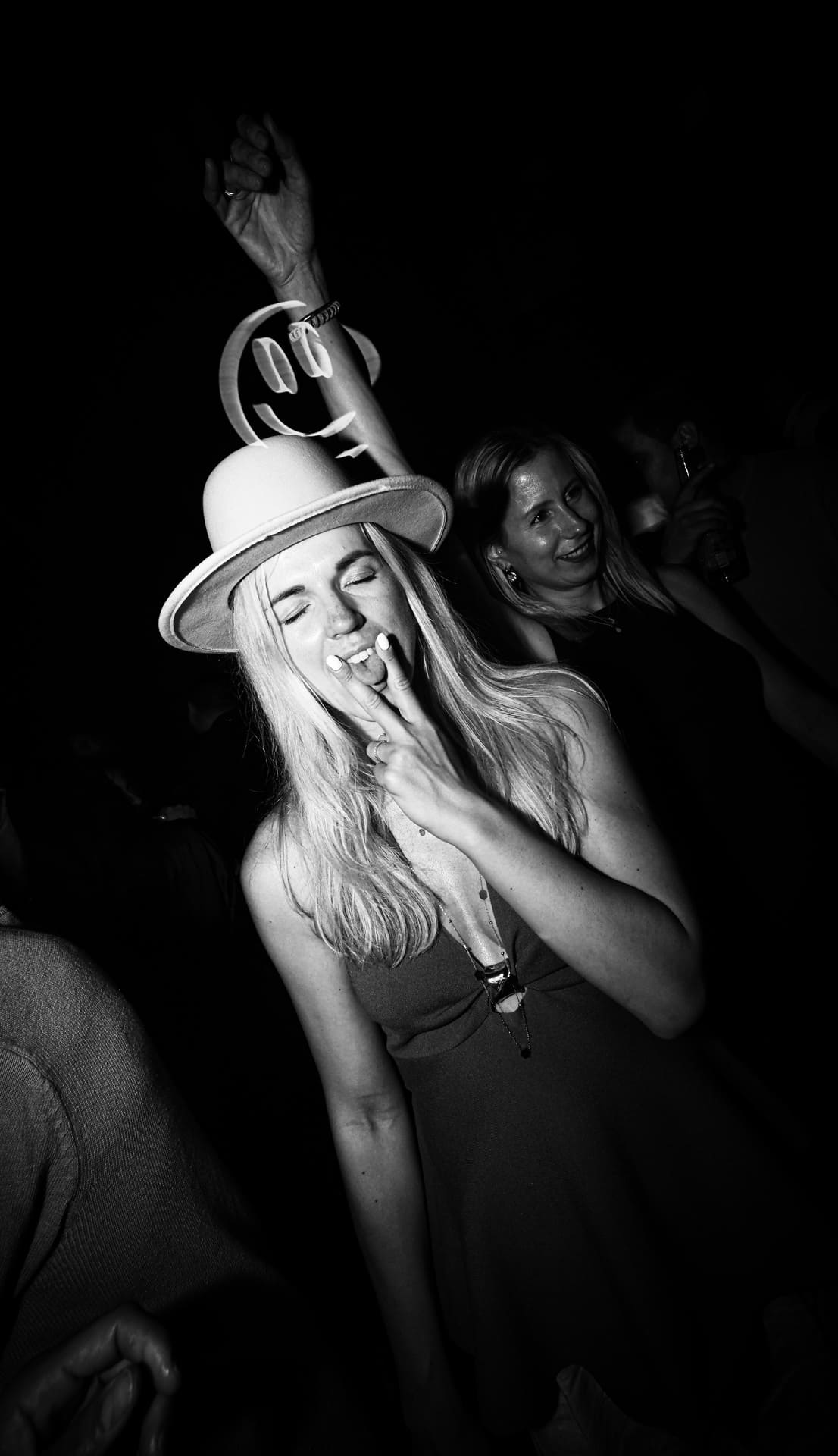 Woman wearing a hat and making a peace sign while dancing at a nightclub.